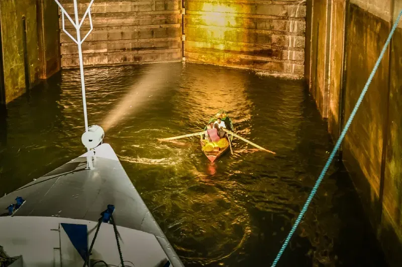 La chiusa di Esna sul fiume Nilo di notte: una piccola barca a remi appare illuminata dal potente fascio di luce di una nave da crociera.