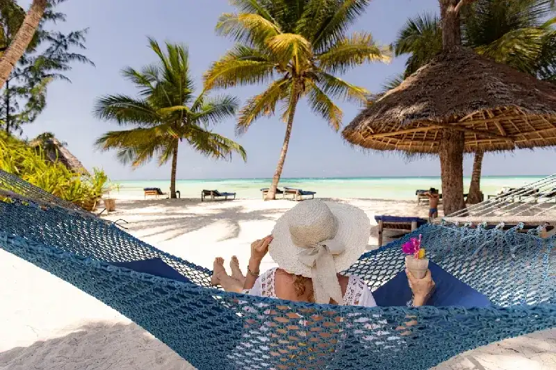Woman relaxing in a hammock on a Zanzibar beach with a smoothie.