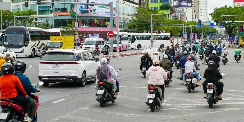 Decenas de motociclistas atraviesan un bullicioso cruce urbano en Da Nang.