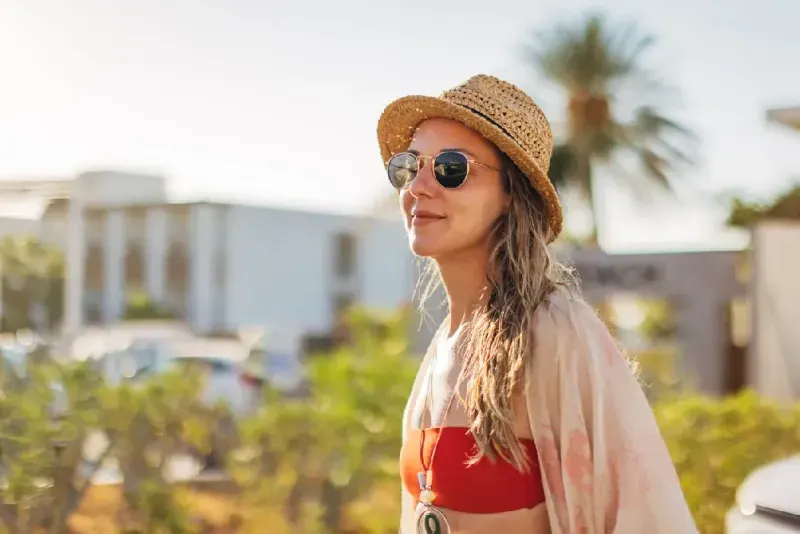 mujer-sonriente-con-gafas-caminando-por-la-calle-rumbo-a-la-playa