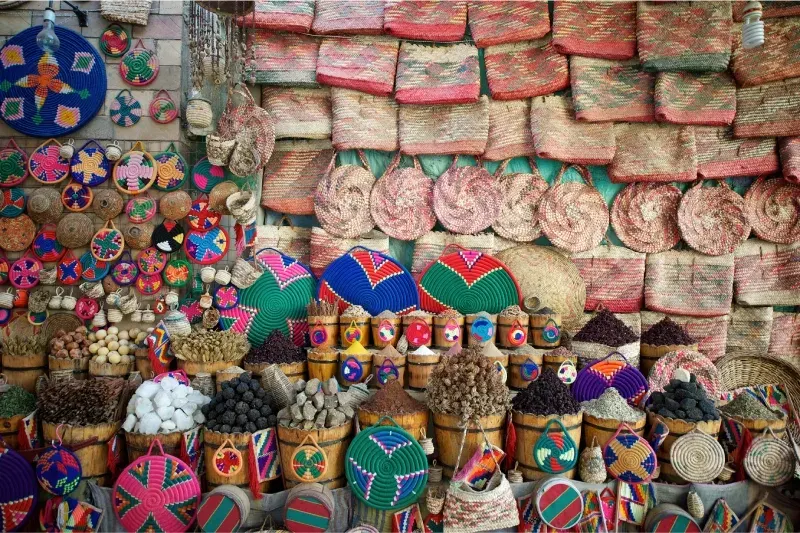 Borse intrecciate colorate e cumuli di spezie aromatiche in una bancarella del souk di Assuan, Egitto.