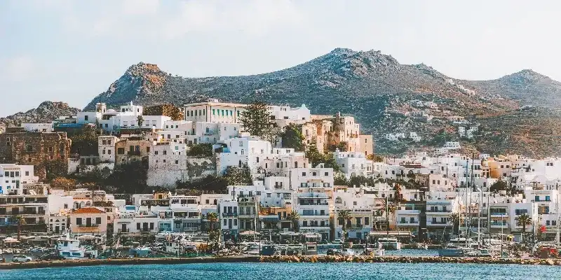 Vista panorámica de la ciudad de Naxos, donde los edificios encalados, adornados con coloridas ventanas, se yerguen imponentes contra el brillante sol mediterráneo de fondo.