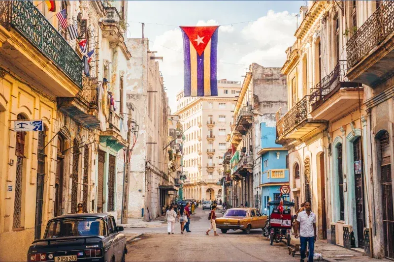 Straße in Havanna mit kubanischer Flagge zwischen historischen Gebäuden.