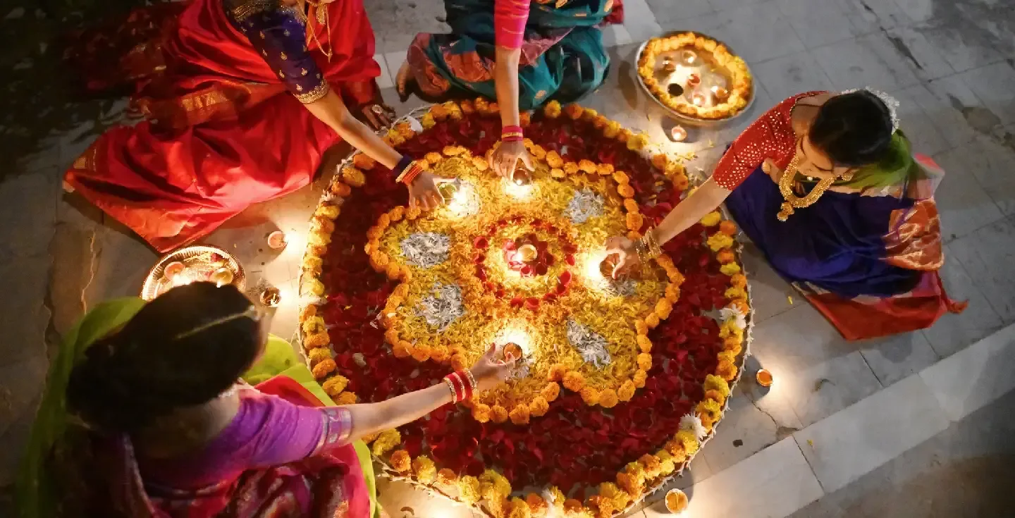 Mujer india vestida con un traje tradicional festivo, decorando Rangoli con lámparas de aceite (Diya), sentada cerca de un templo en un palacio de Rajastán.