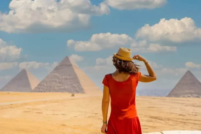 A tourist lady in red dress is standing in front of the great pyramids in Giza  