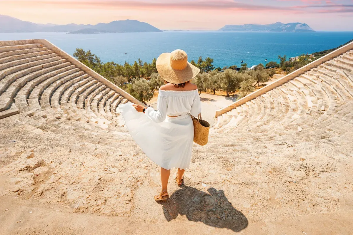 gorgeous-woman-in-white-dress-and-hat-explores-ancient-landmark-and-ruins-of-Greek-or-Roman-amphitheater