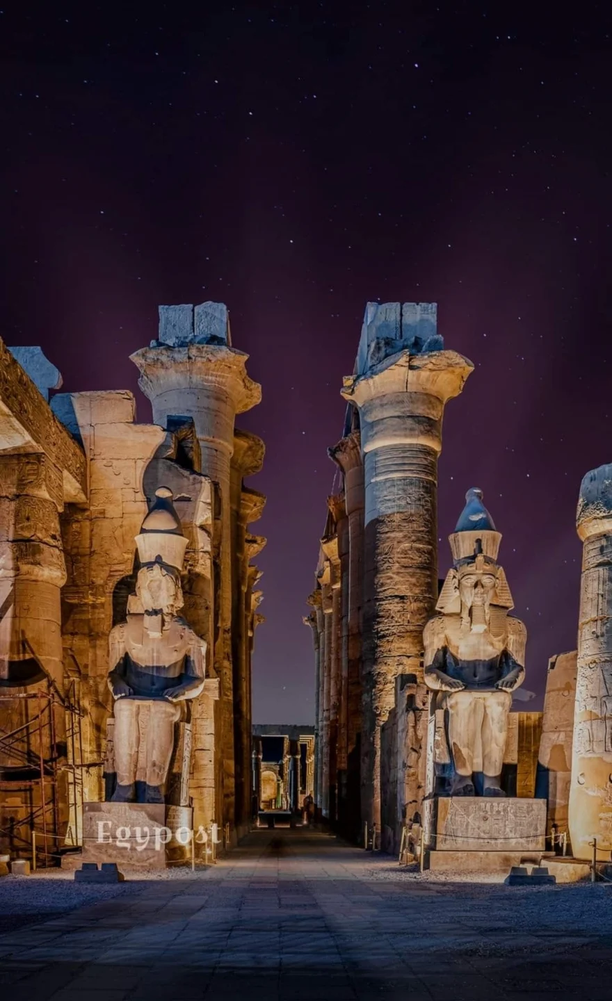 Illuminated statues and columns of Luxor Temple in Egypt glowing at night with a clear, star-filled sky above.