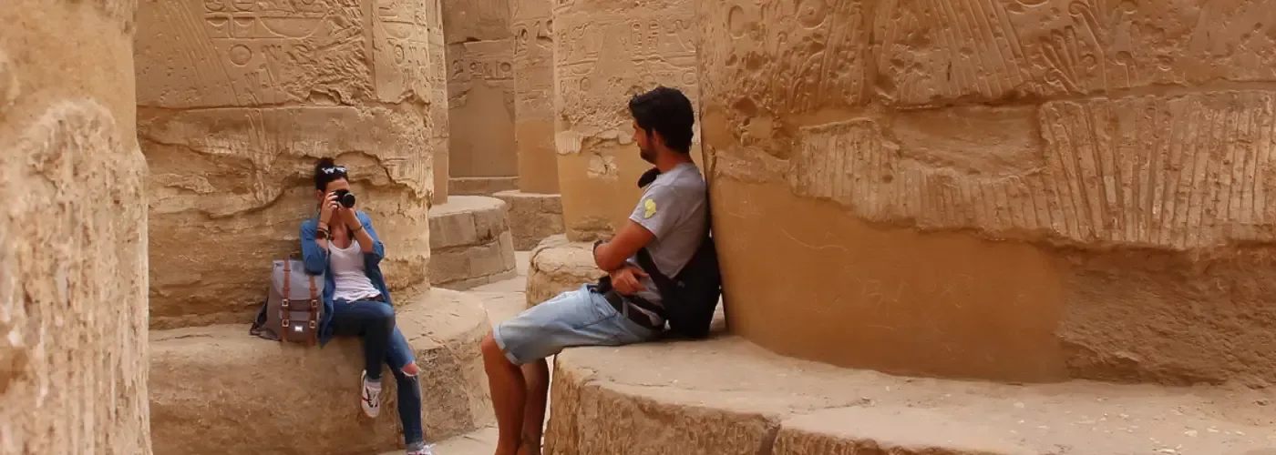 Due turisti tra le monumentali colonne decorate con geroglifici nel Tempio di Karnak in Egitto, intenti a fotografare.