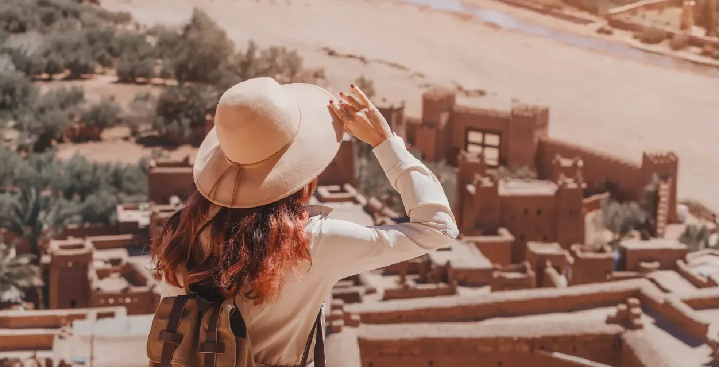 Turista femenina sosteniendo su sombrero y admirando el paisaje sobre Ait Benhaddou Ksar, una antigua ciudad fortificada en Marruecos.