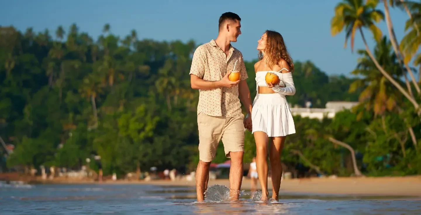 Una pareja romántica camina por una soleada playa tropical, bebiendo agua de coco fresca.