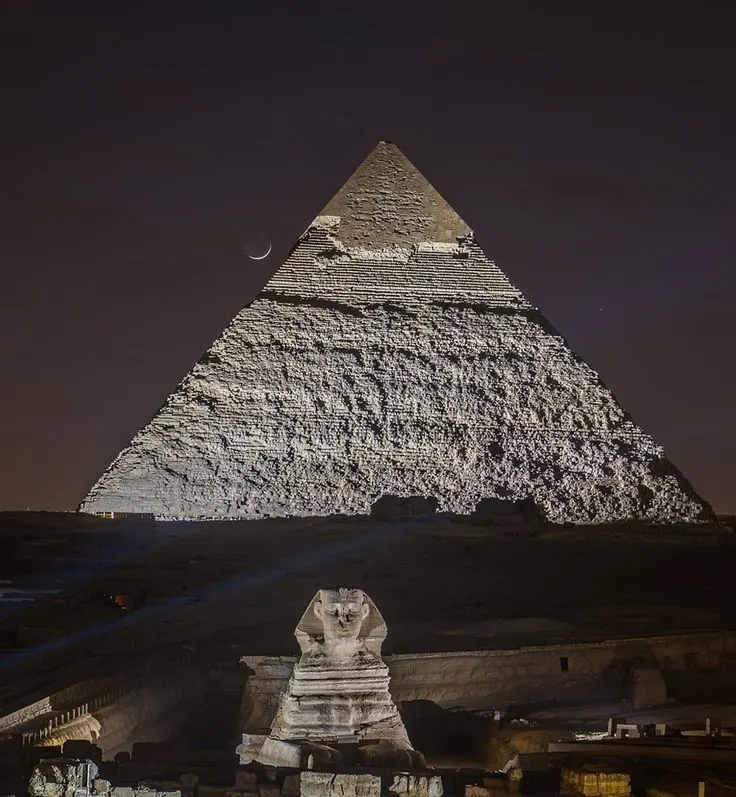 Night view of the Great Pyramid of Giza illuminated with the Sphinx in the foreground and a crescent moon in the sky