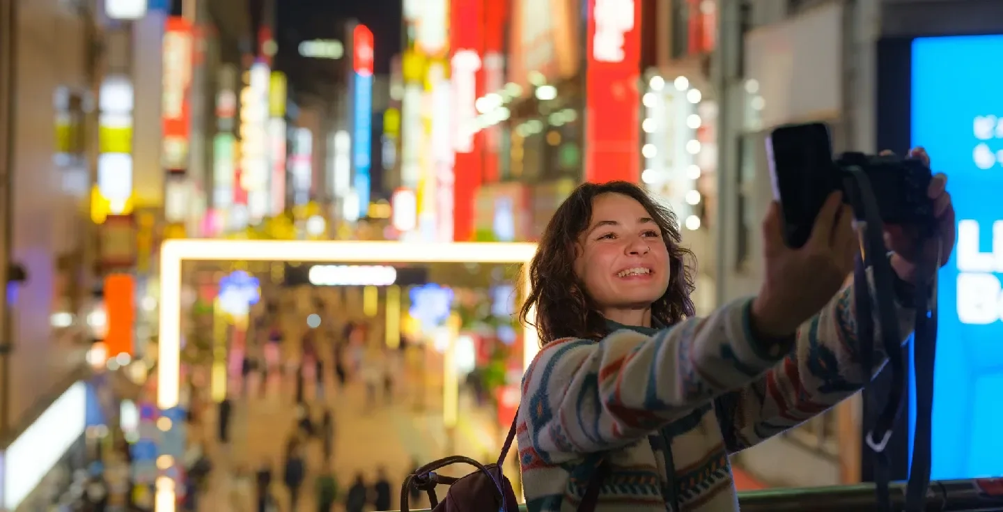 una mujer alegre con el bullicioso barrio de Shinjuku de fondo durante su viaje de inmersión cultural a Tokio, Japón.