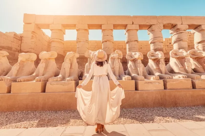 a woman tourist in beige dress stand in front of Karnak temple
