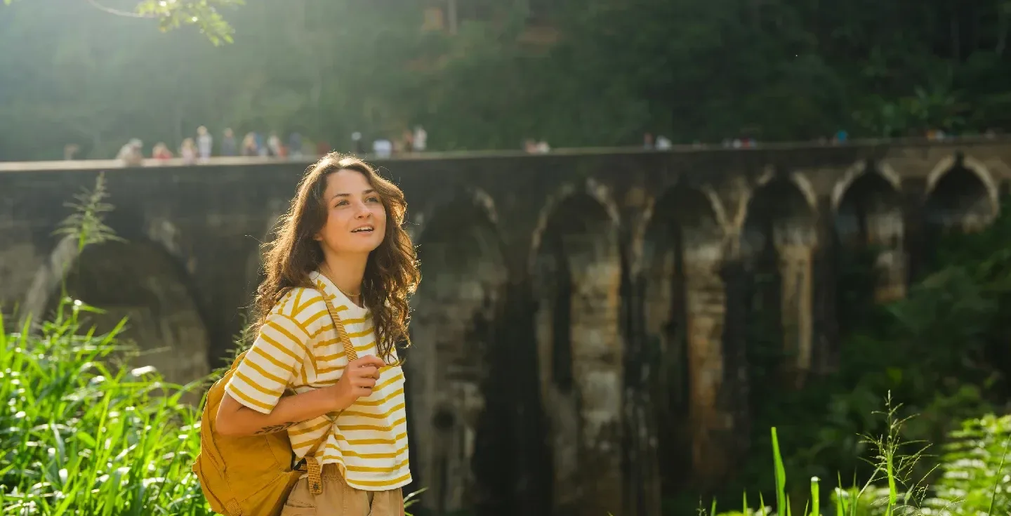 Mujer alegre de pie cerca del puente de nueve arcos en Sri Lanka al atardecer.