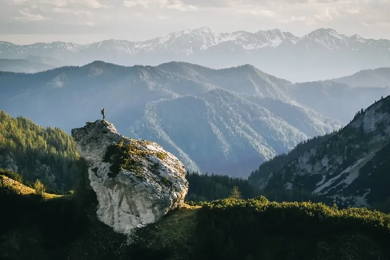 Wanderer entspannt auf einem Berggrat bei Sonnenaufgang mit weitem Blick über die Berglandschaft