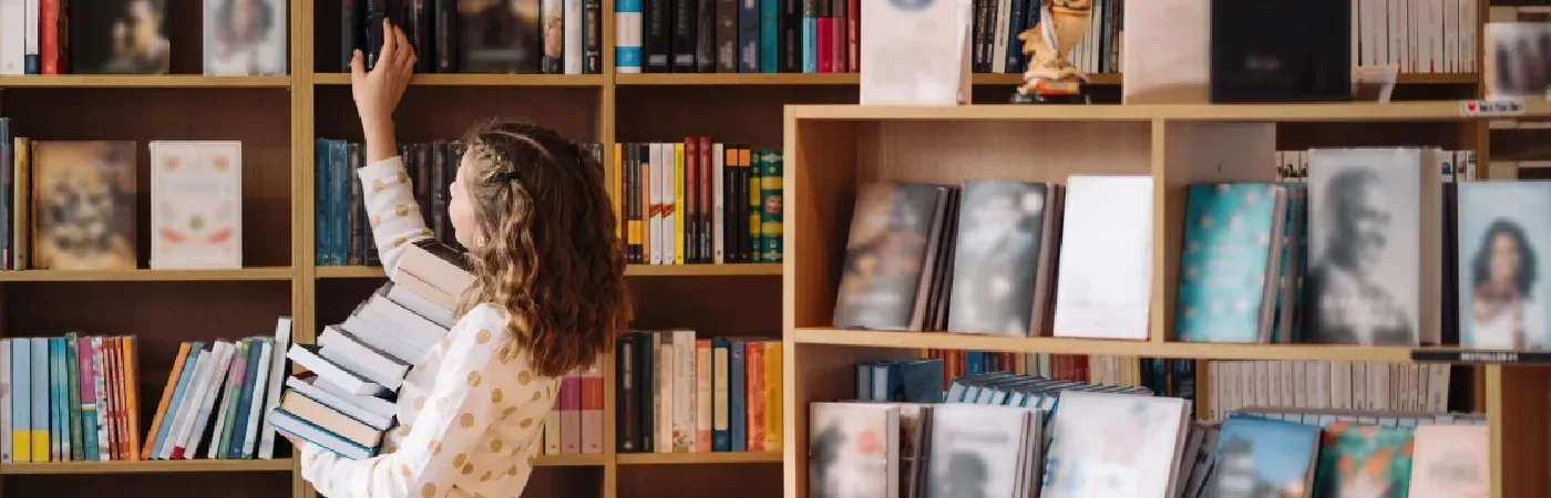 Teenager zwischen einem Bücherstapel. Ein junges Mädchen, das Bücher hält, mit Regalen im Hintergrund. 