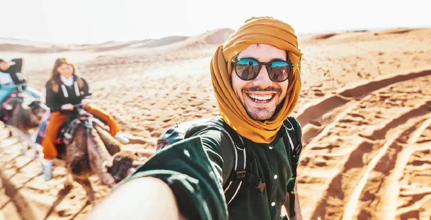 Turista feliz disfrutando de un paseo en camello en grupo por el desierto.