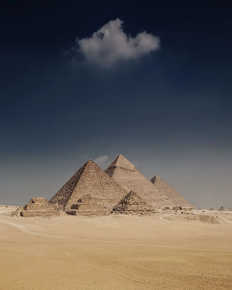 View of the Pyramids of Giza in Egypt with a dark sky and a single cloud above the desert