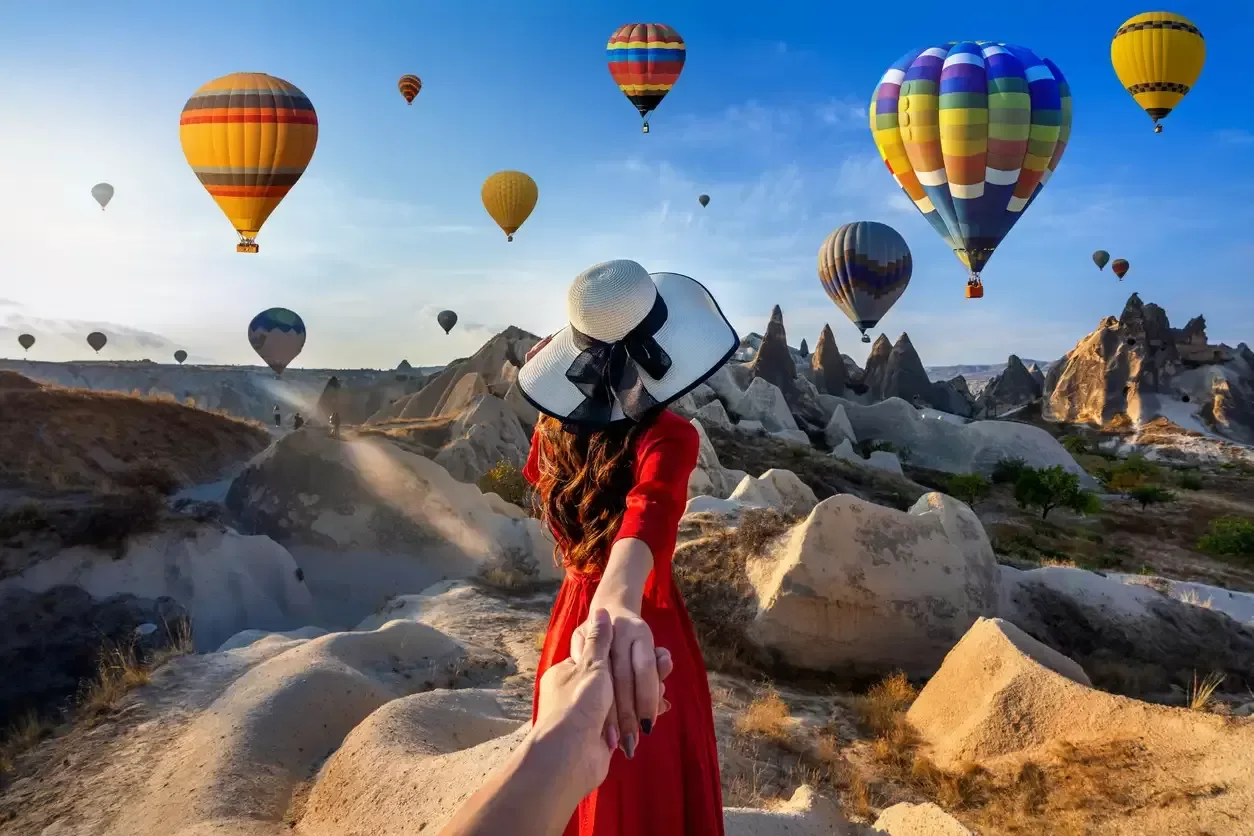 New York woman holding partner’s hand toward hot air balloons in Cappadocia.