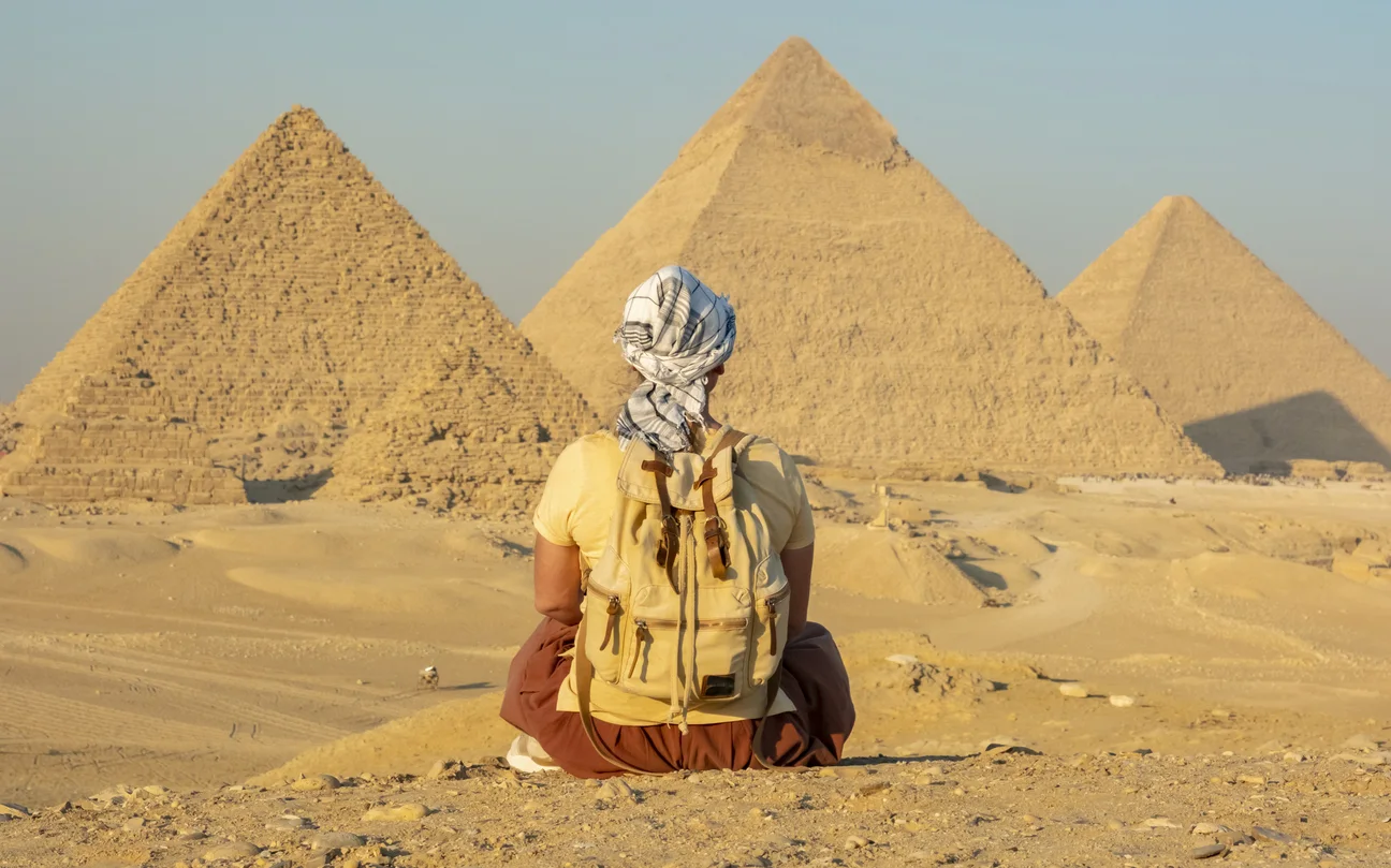 Person sitting on sand looking at the pyramids in Giza plateau, Best Time to Visit Egypt