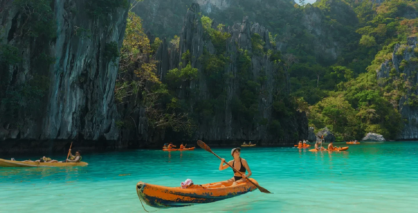 Woman kayaking on the turquoise waters of El Nido in Palawan, Philippines, with towering limestone cliffs and tropical scenery.