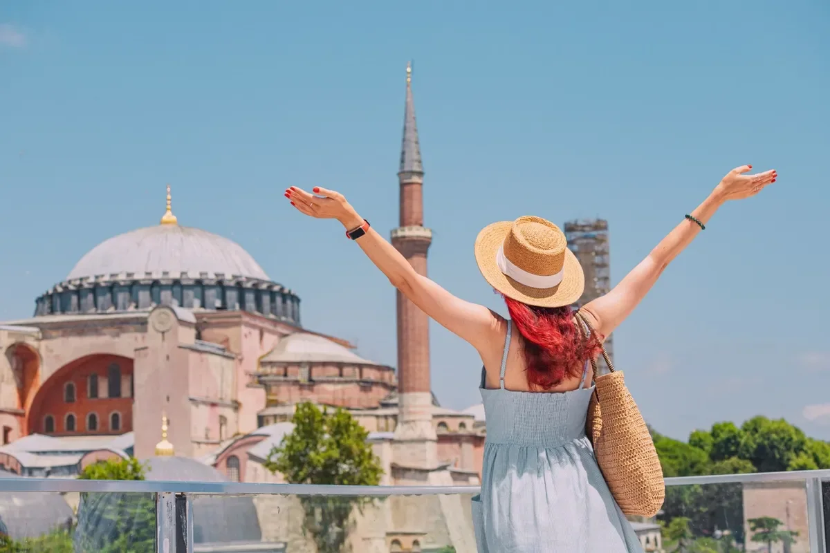 Woman in a sun hat raising her arms in front of the Hagia Sophia in Istanbul, Turkey