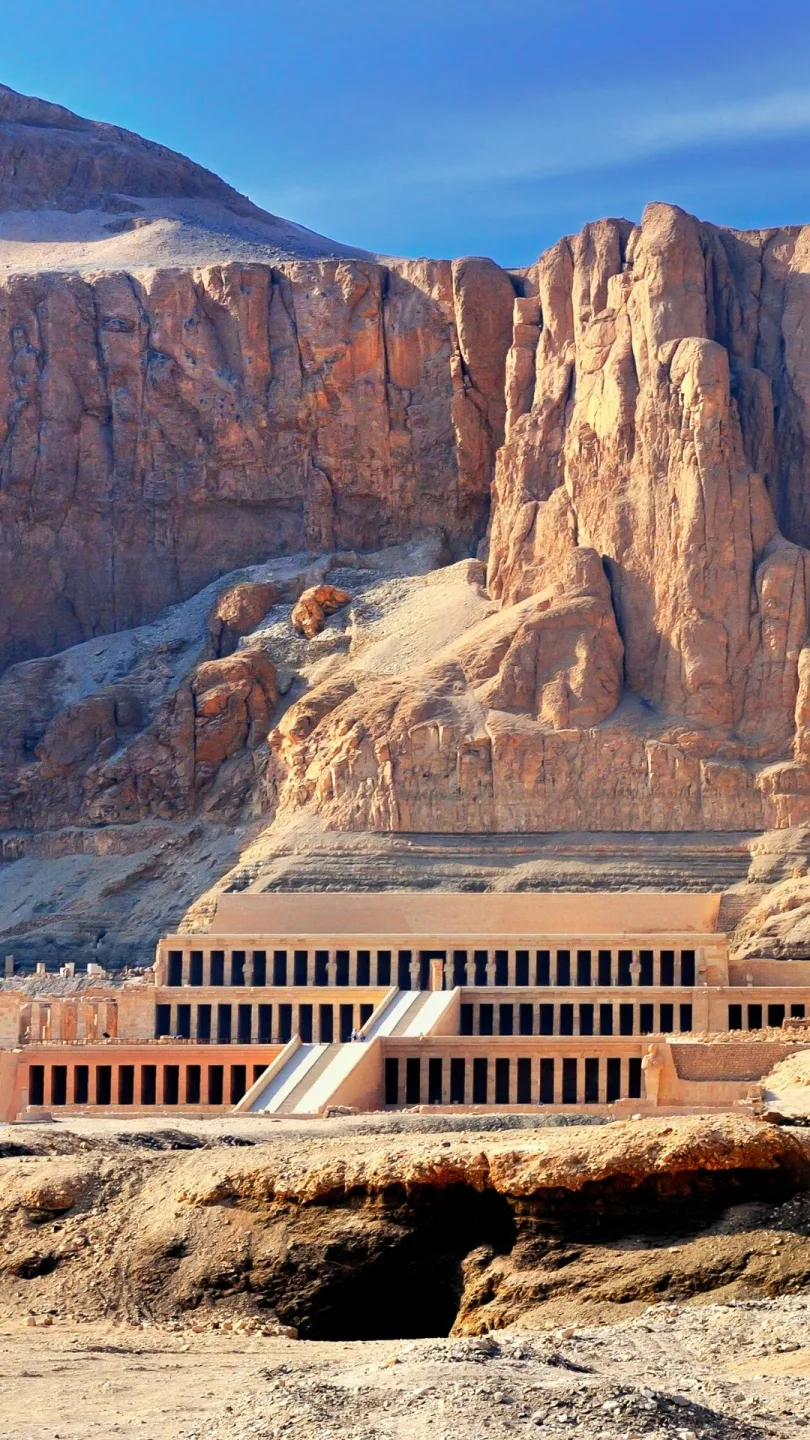  A frontal view of the Mortuary Temple of Hatshepsut, built into the cliffs of Deir el-Bahari in Luxor, Egypt, under a clear blue sky.