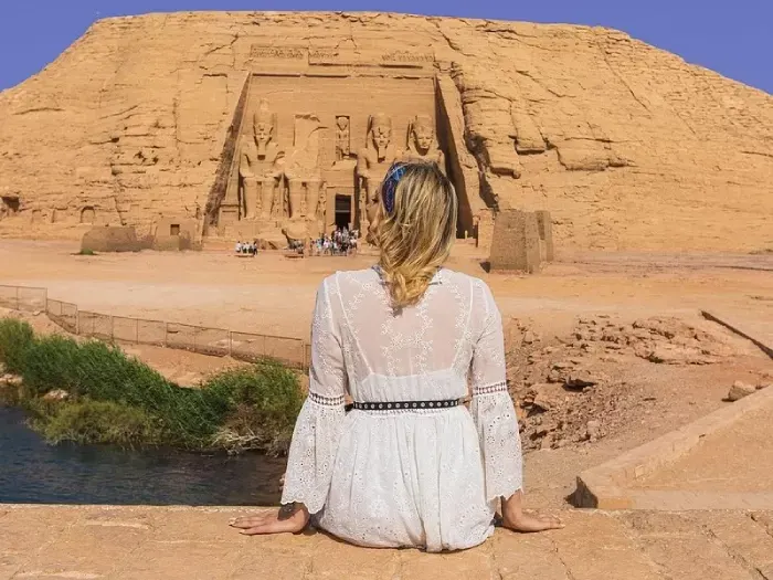 a blonde lady in white dress is setting infront of Abu Simble temple 