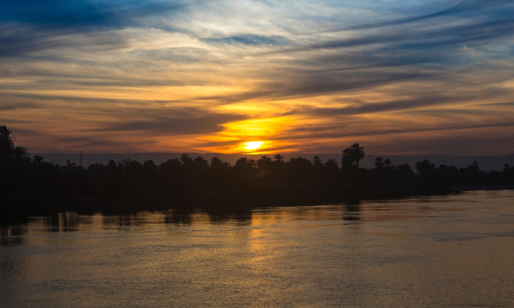 Sonnenuntergang über dem Nil mit Palmensilhouetten am Ufer
