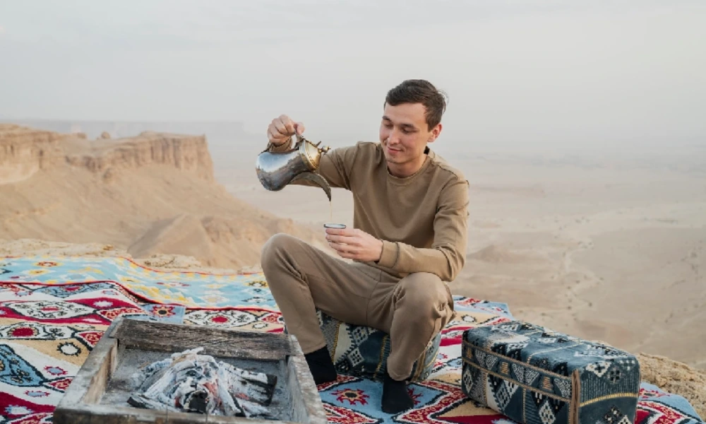 Mann schenkt arabischen Kaffee auf einem Teppich in der Wüste ein