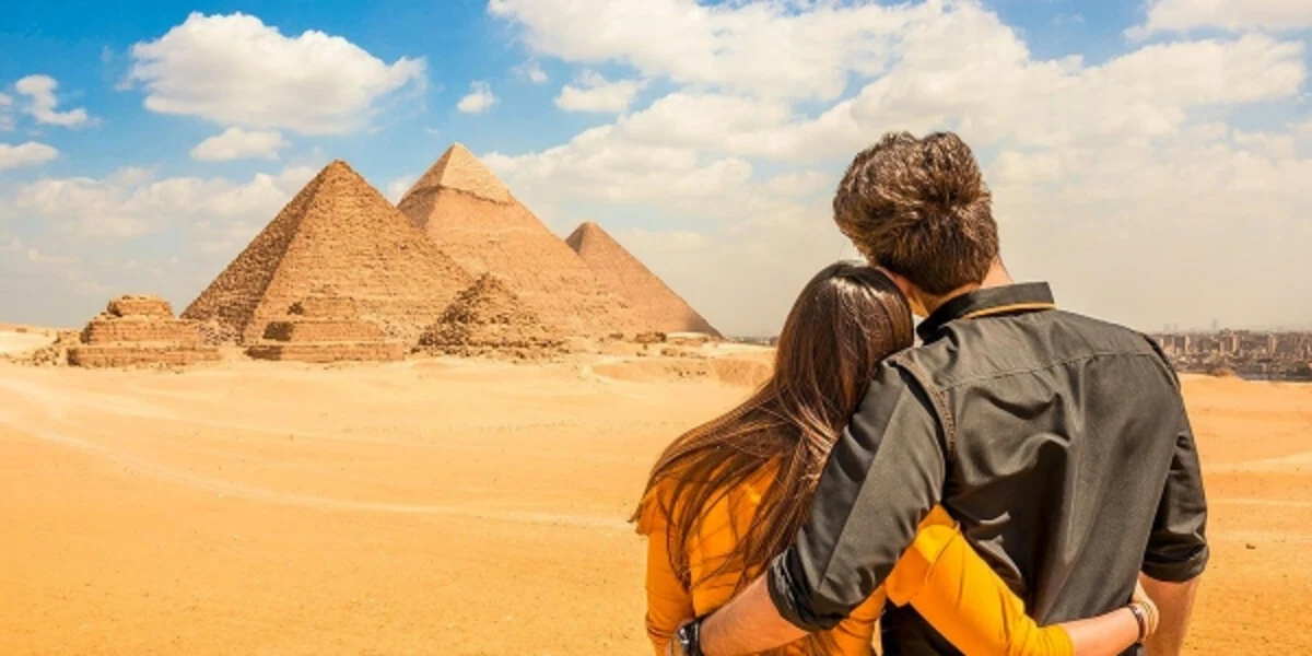 Couple embracing as they admire the Pyramids of Giza under a partly cloudy desert sky.