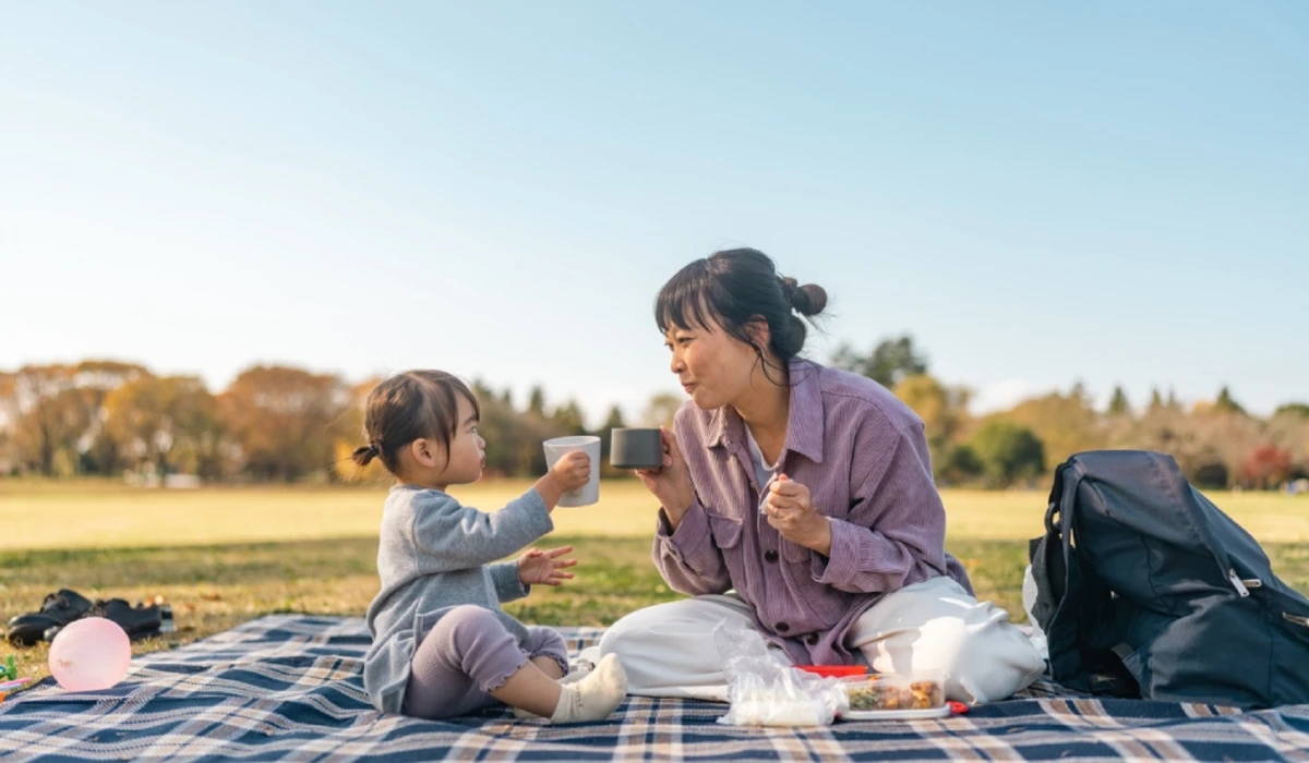 Adult and child clinking cups at autumn picnic.
