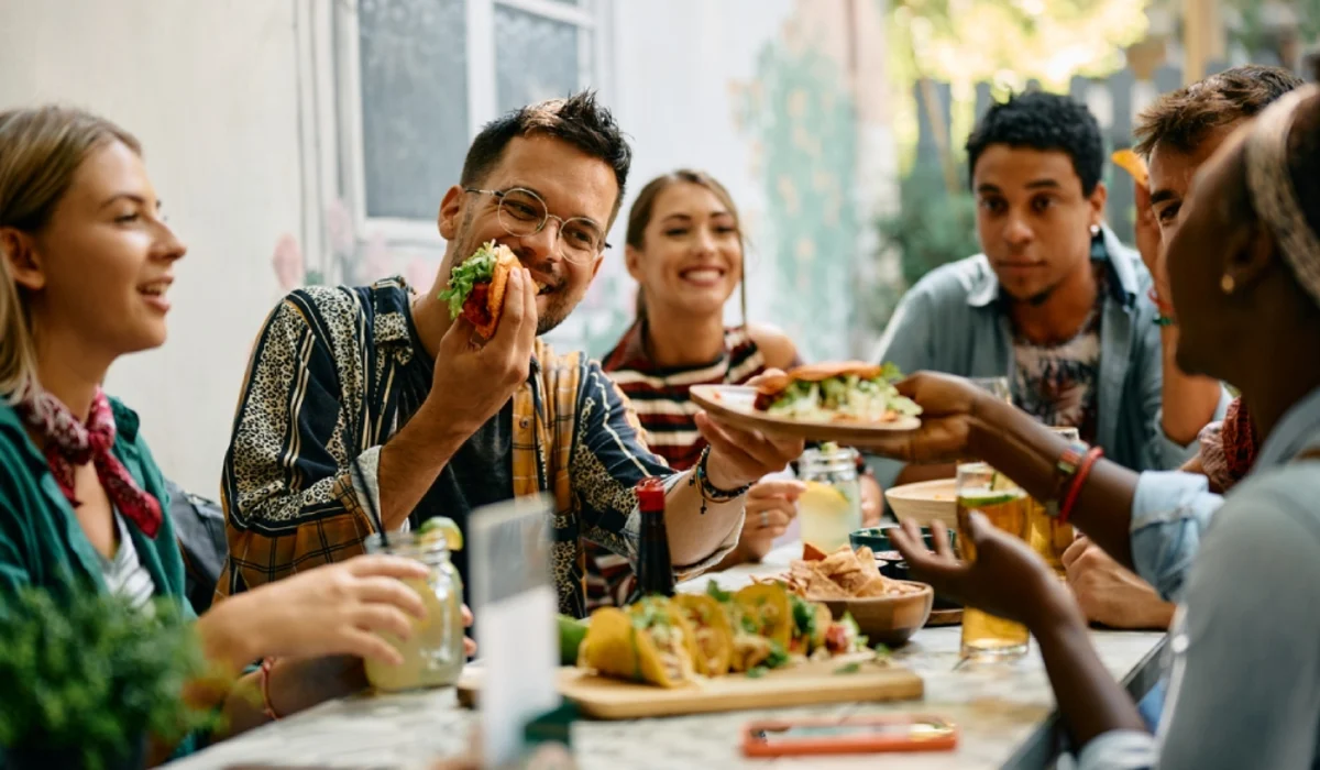 Group of friends sharing tacos at outdoor lunch table.