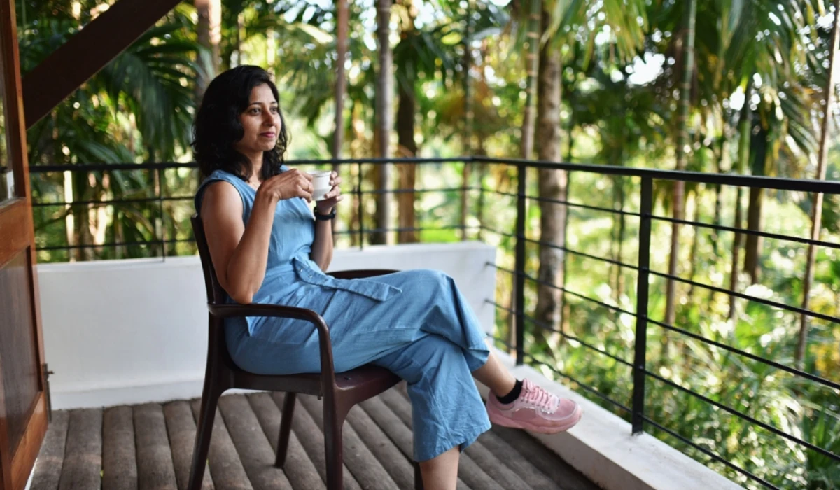 Person relaxing on balcony with drink amid tropical greenery.
