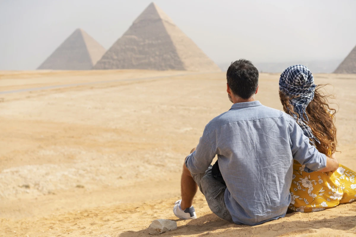 Paar sitzt auf einer Düne und blickt auf die Pyramiden von Gizeh