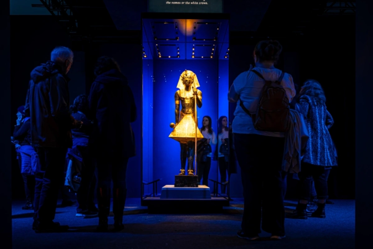 Besucher vor einer vergoldeten Wächterstatue des Tutanchamun in einer abgedunkelten Ausstellung