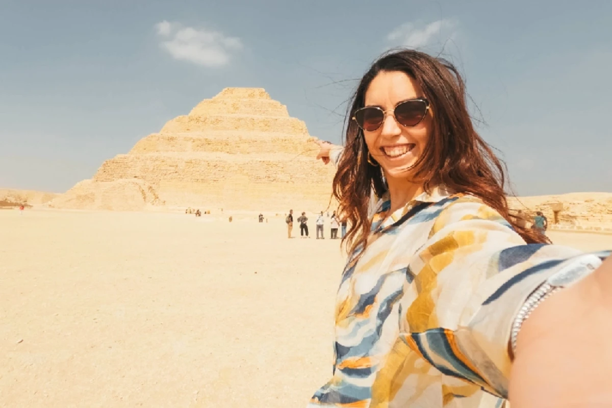 Junge Frau macht ein Selfie in der Sakkara-Wüste vor der Stufenpyramide des Djoser.