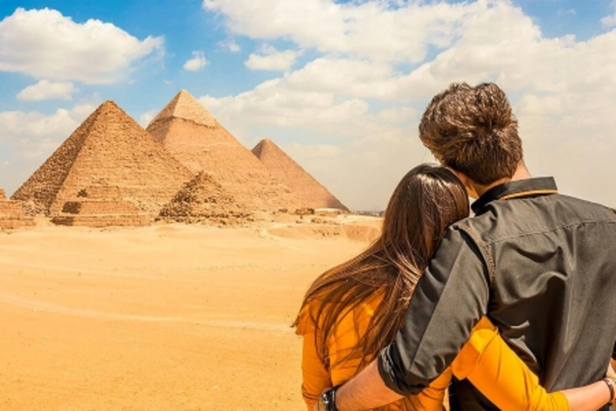 Couple embracing as they admire the Pyramids of Giza under a partly cloudy desert sky.
