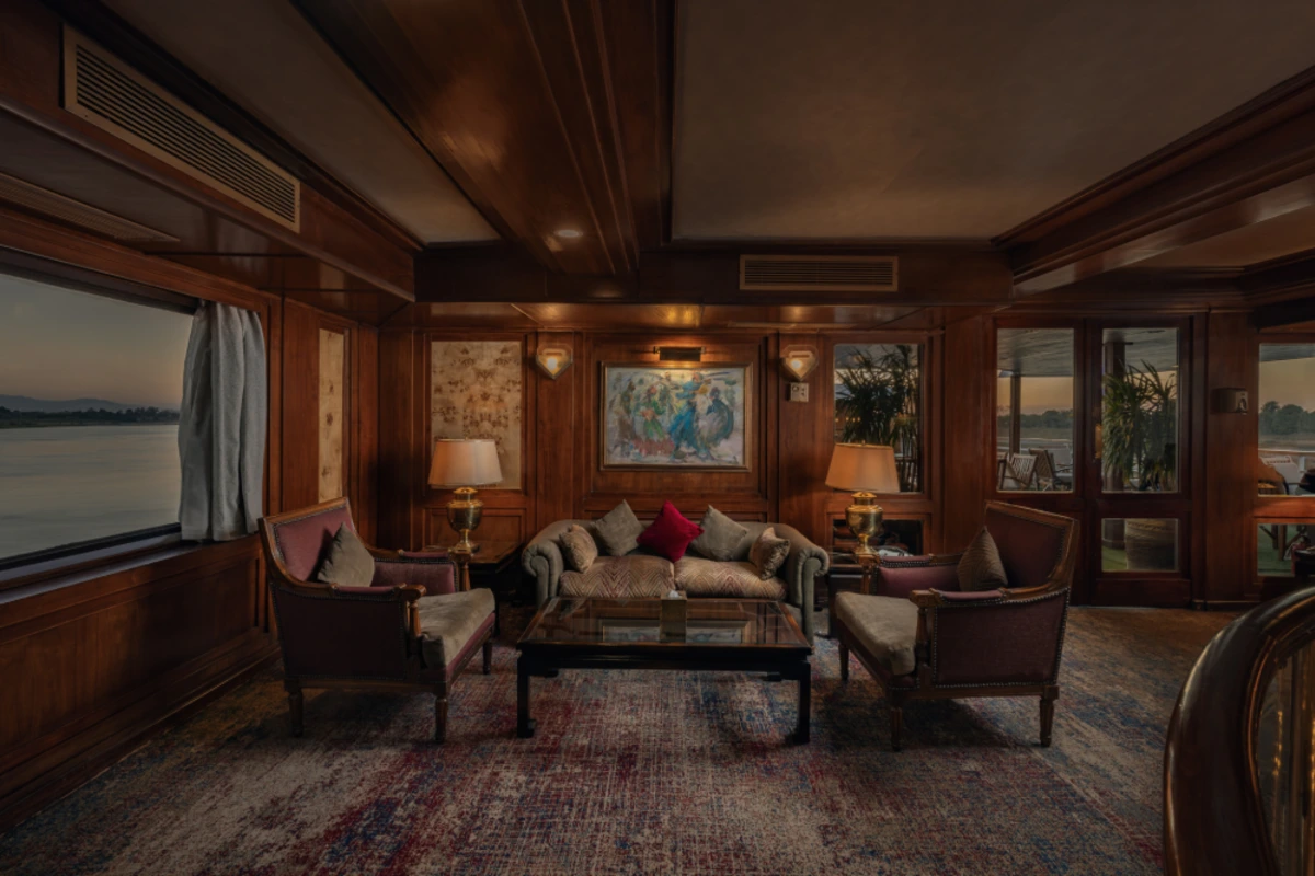 Luxurious lounge with velvet armchairs, gold-accented lamps, and a large window overlooking serene waters.