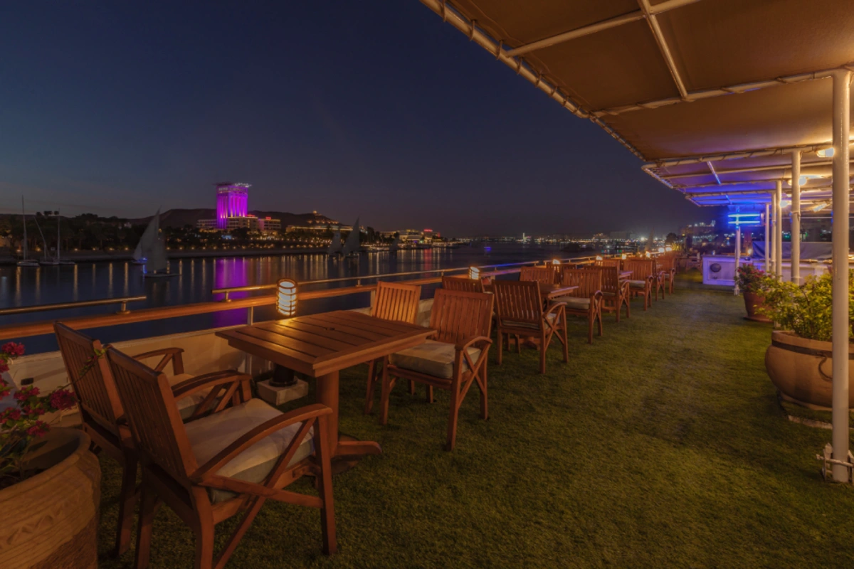 Outdoor terrace dining area at night with lantern-lit tables, river views, and a cityscape illuminated across the water.