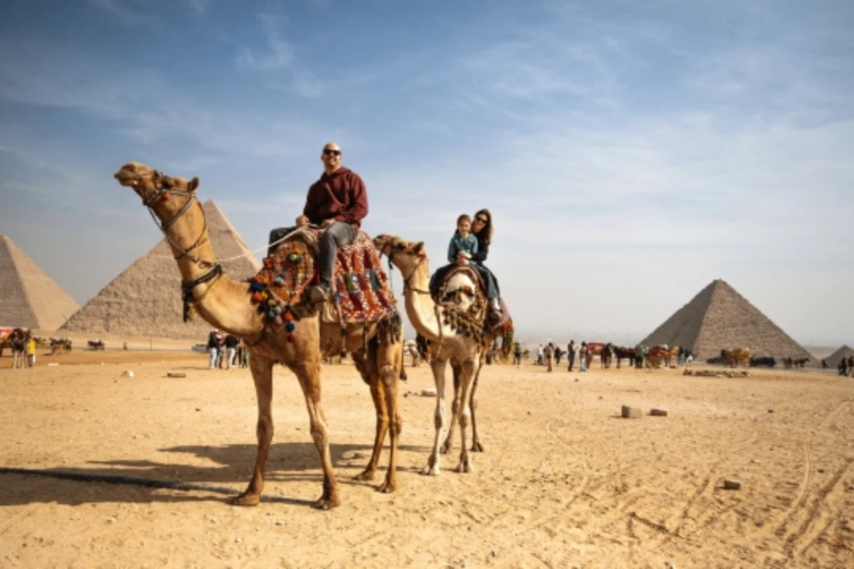 Tourist family riding camels in a vast desert landscape under a clear blue sky, Egypt Cairo to Luxor