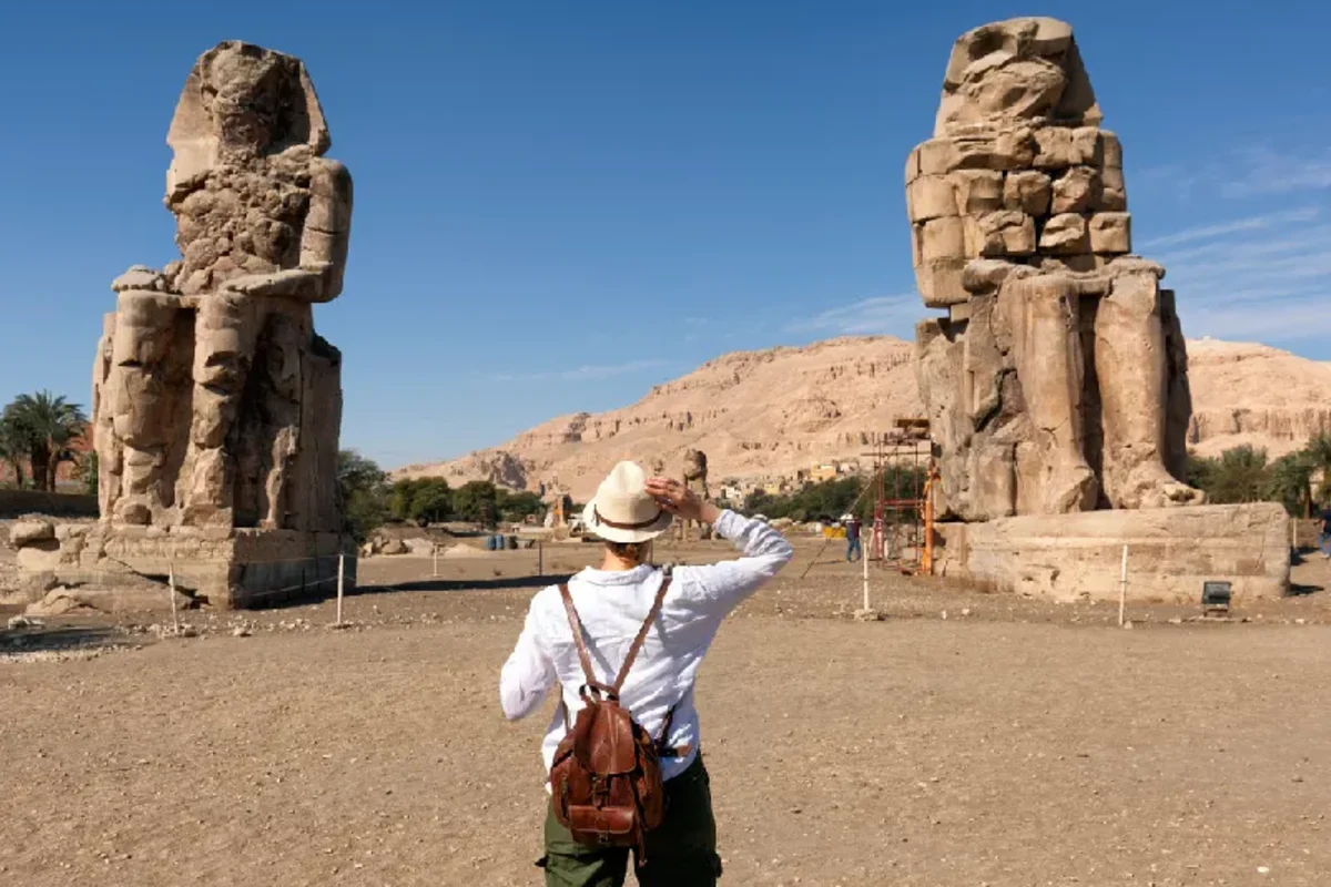 Turista interesada en la egiptología y la arqueología junto a los Colosos de Memnón, las estatuas del faraón Amenhotep III en Luxor, Viaje a Egipto Todo Incluido