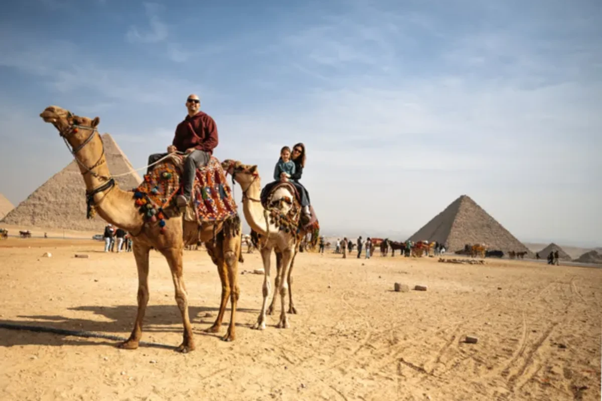 Familia de turistas montando en camello en un amplio paisaje desértico bajo un cielo azul despejado, Tour Egipto