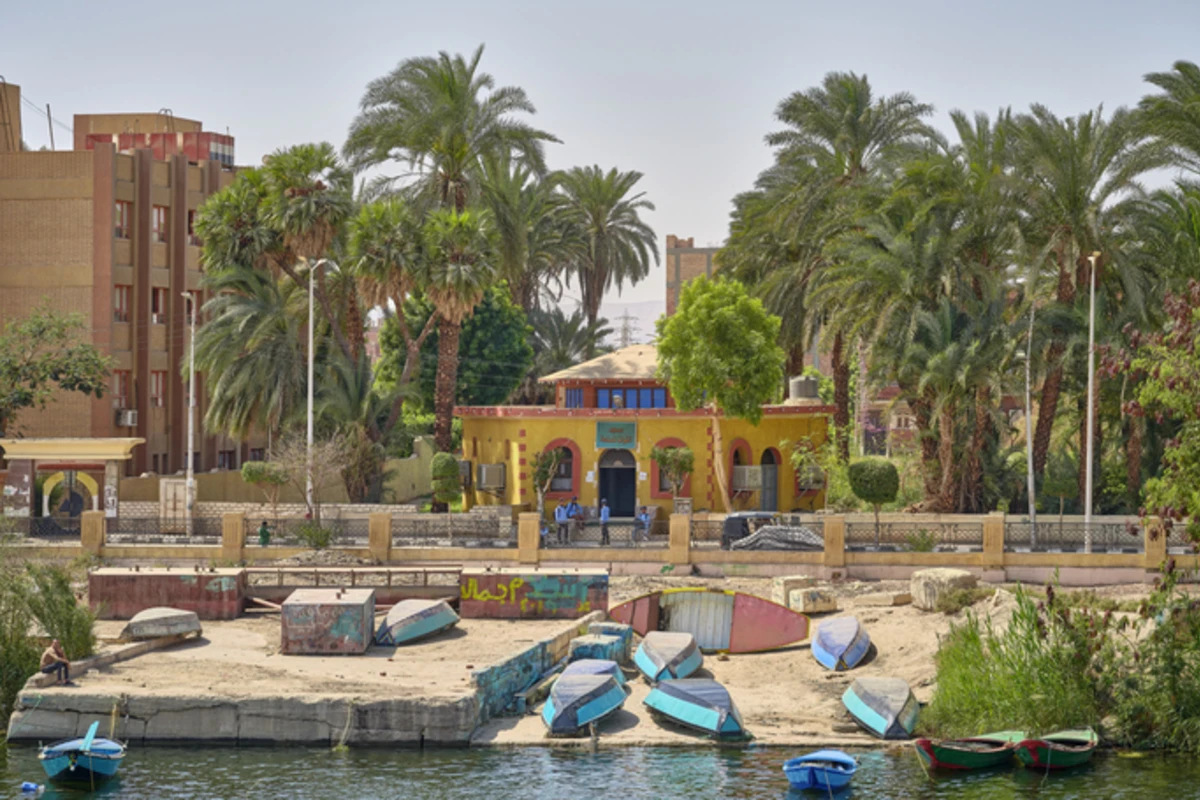 Bateaux colorés au bord du Nil, avec un bâtiment jaune et des palmiers en Égypte, Circuit égypte 10 jours