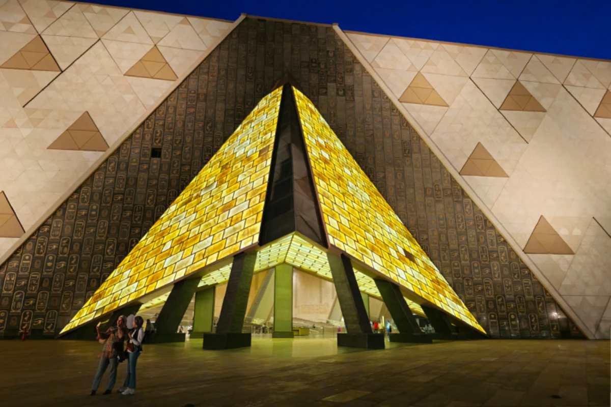 Beleuchteter Eingang des Grand Egyptian Museum bei Nacht mit moderner Pyramidenarchitektur und Besuchern