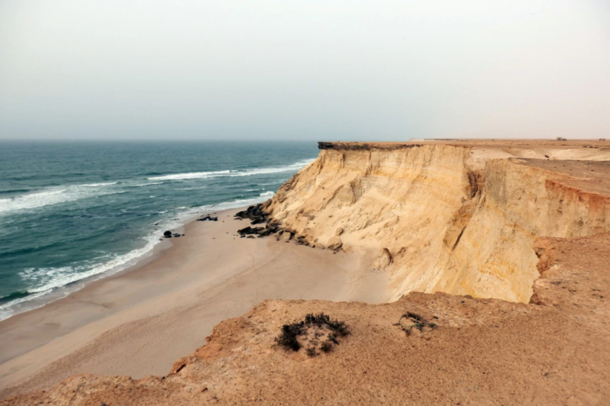 Weite Küstenlandschaft mit Sandstrand, Klippen und türkisem Meer.