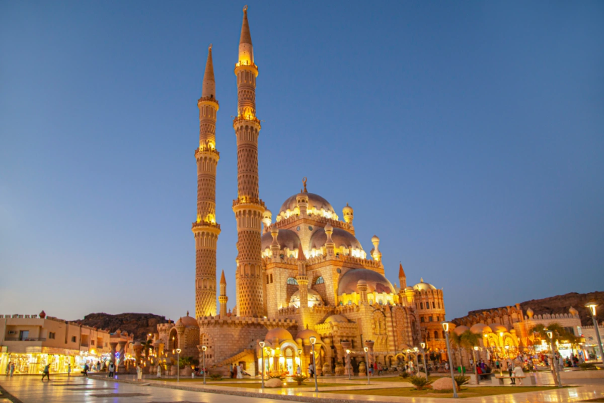 Al-Sahaba-Moschee in Sharm El Sheikh bei Nacht, gold erleuchtet mit Kuppeln und Minaretten vor einem belebten Platz.
