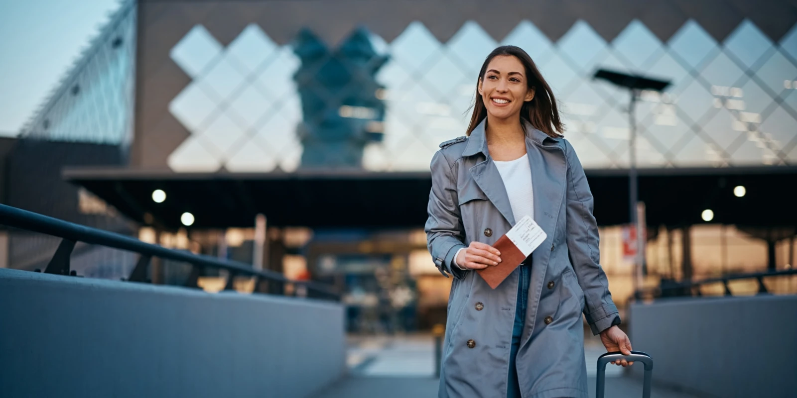 Traveler on an escalator in a modern terminal, holding a coffee cup and suitcase, with glass panels reflecting the scene and other passengers in the background.