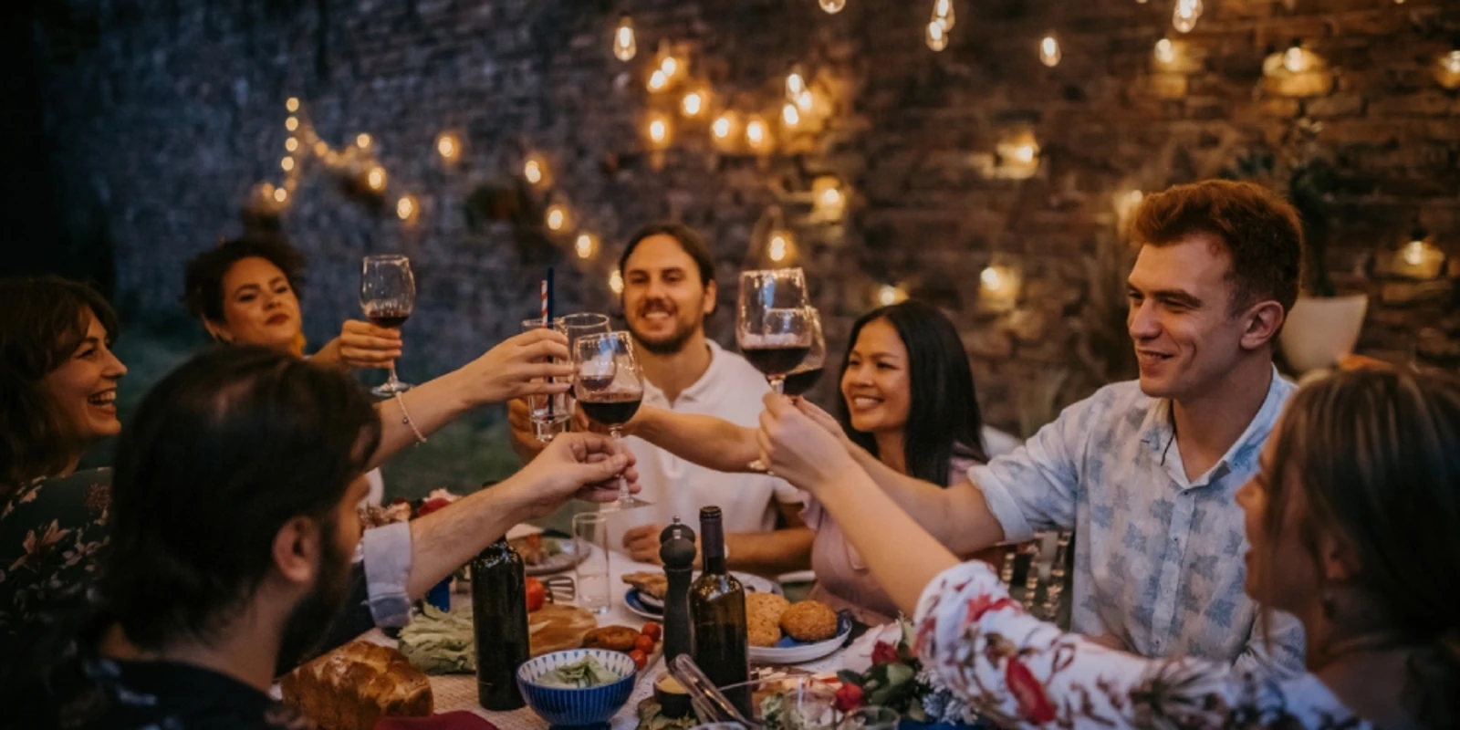 Friends toasting at outdoor evening dinner under string lights.