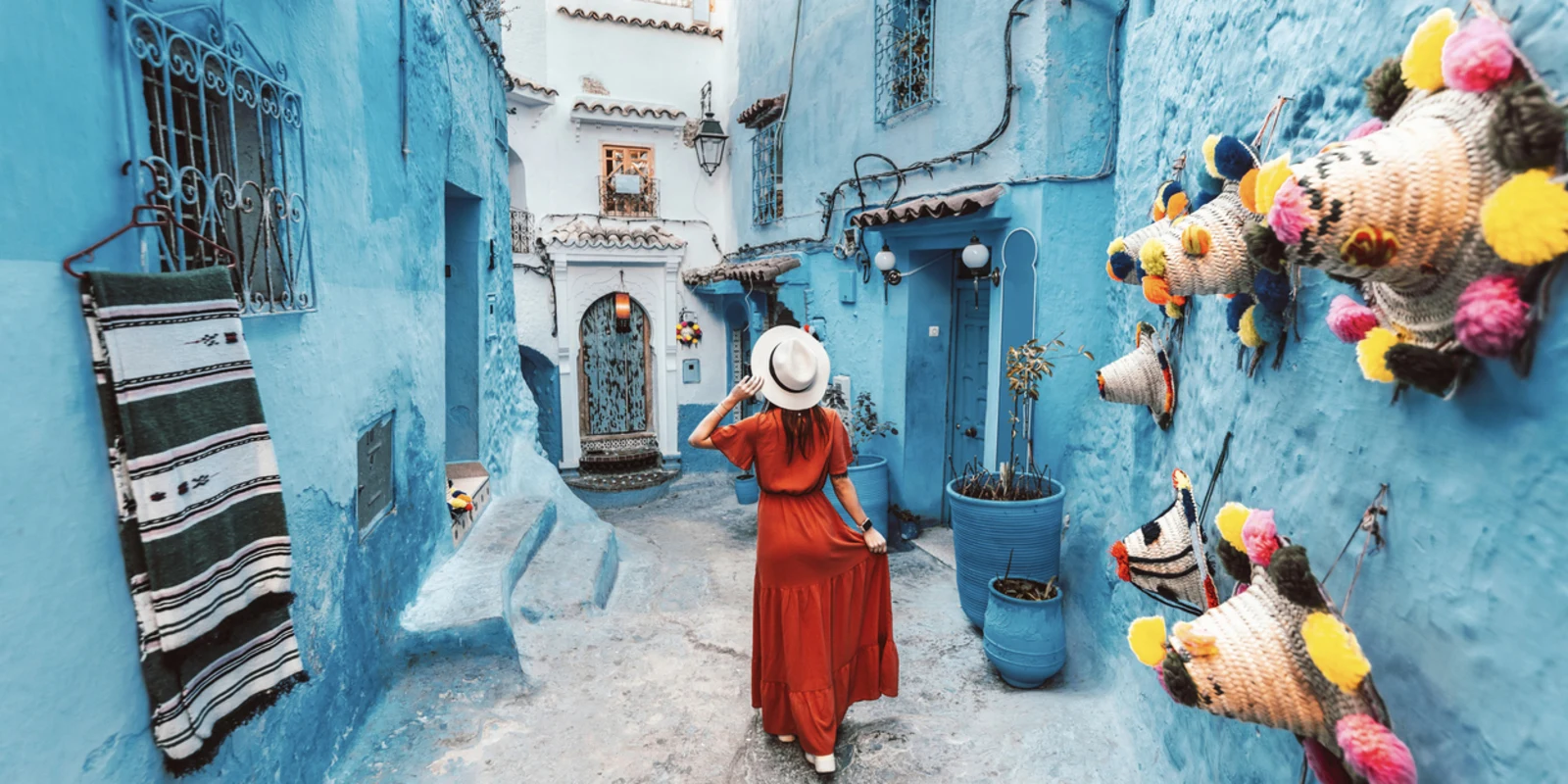 Young woman with red dress visiting the blue city Chefchaouen, Marocco - Happy tourist walking in Moroccan city street - Travel and vacation lifestyle concept